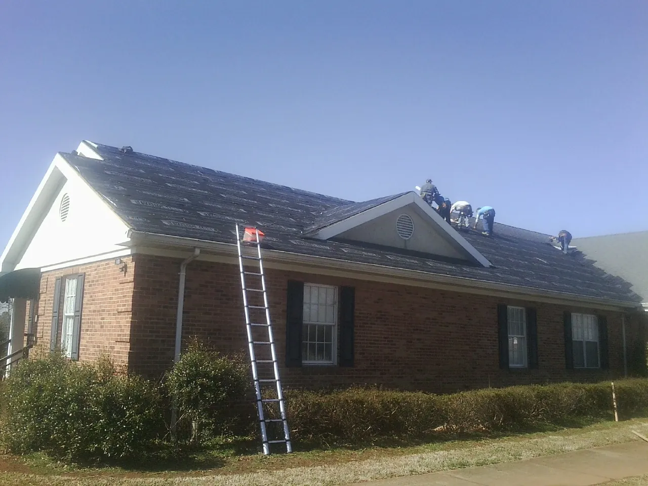Crew tearing shingles off a brick ranch roof with a ladder set — Metal Roof Repair work by our crew in Dearborn