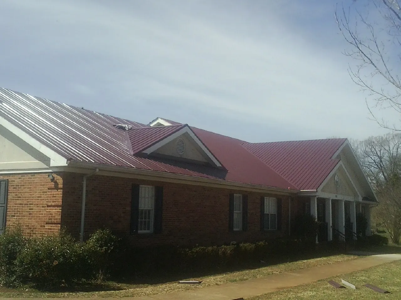 Red metal roof with gabled entries on a long brick building, from a Hail Damage Roof Repair job in Dearborn