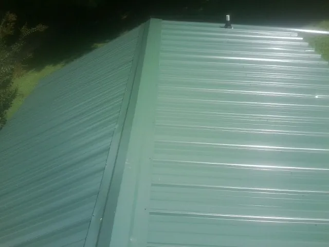New green metal panels meeting at the ridge of a roof — Flat Roof Repair work by our crew in Dearborn